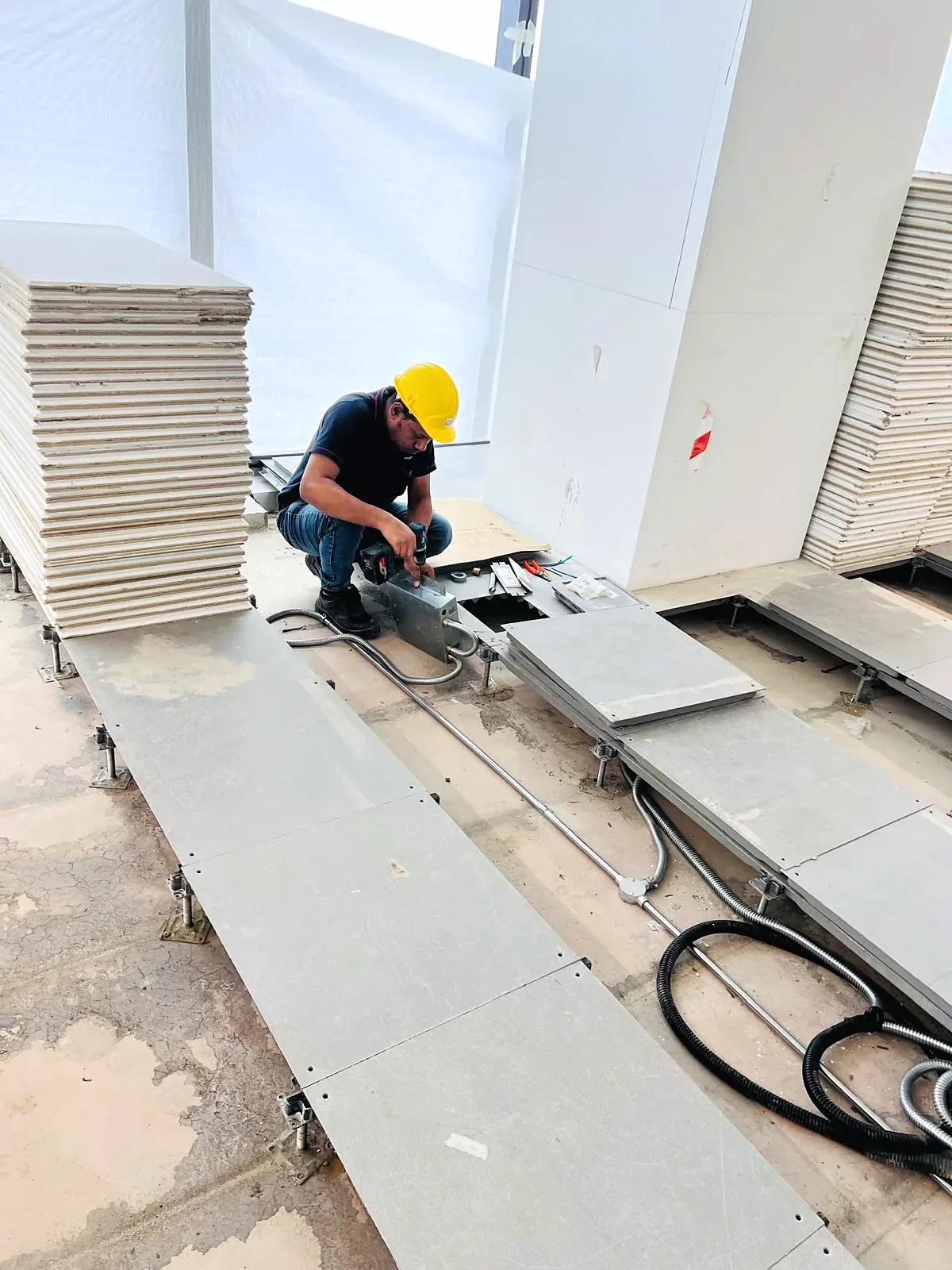 Electrician lifting raised access floor panels to run cabling through the floor void.