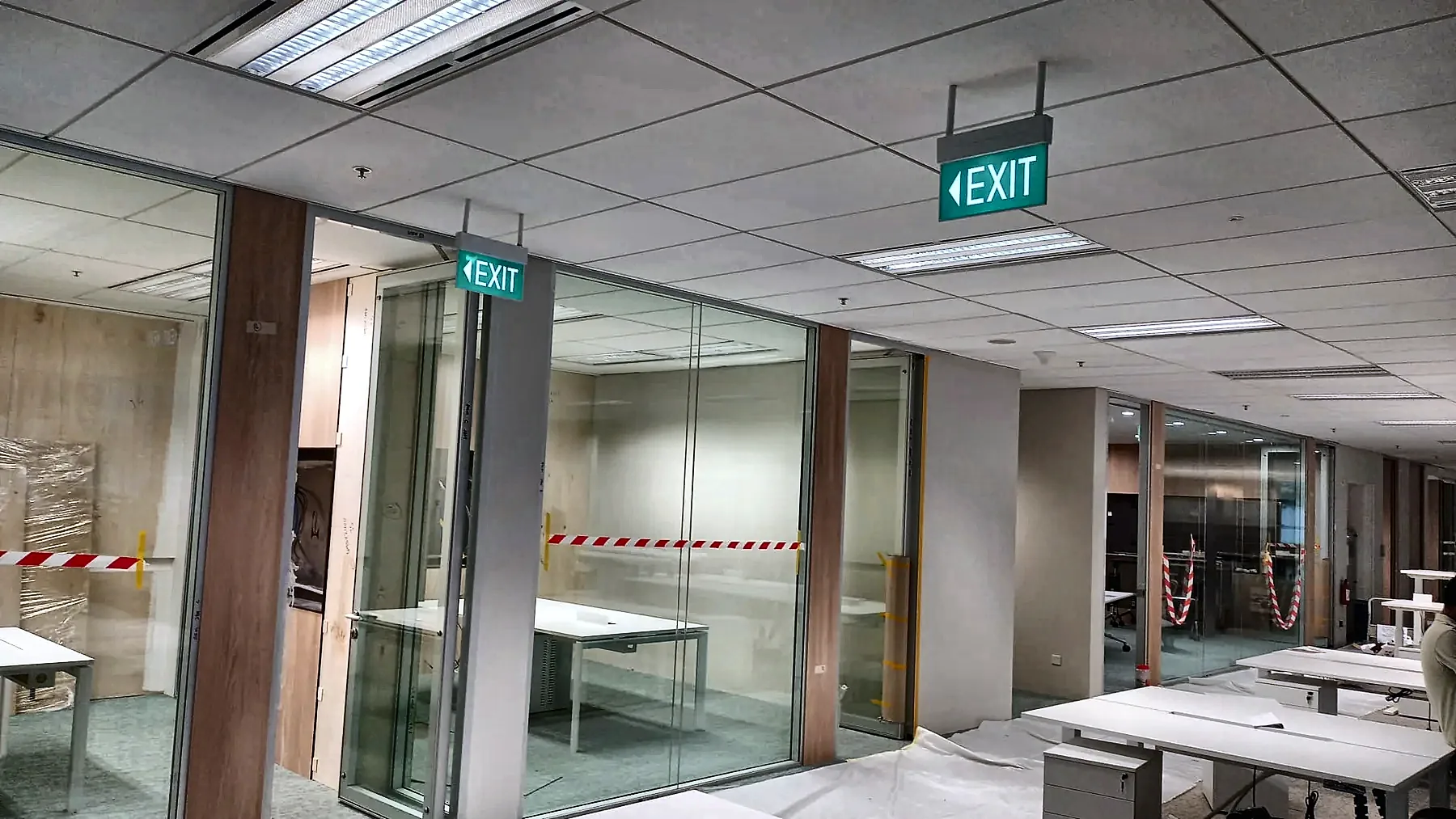 Completed office with recessed ceiling lighting and illuminated emergency exit signage.