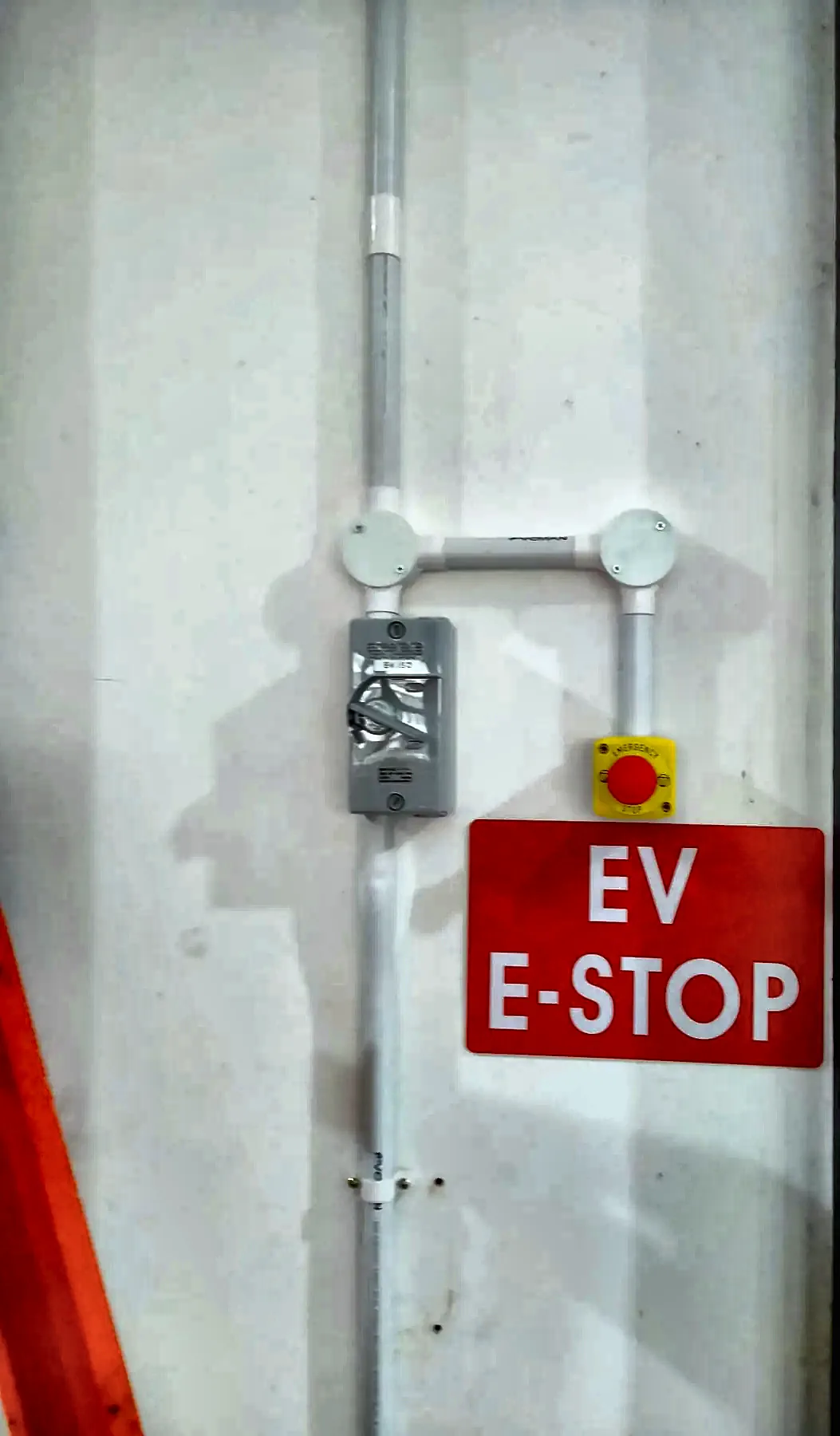 EV emergency stop button with EV E-STOP signage and surface conduit on a commercial wall.