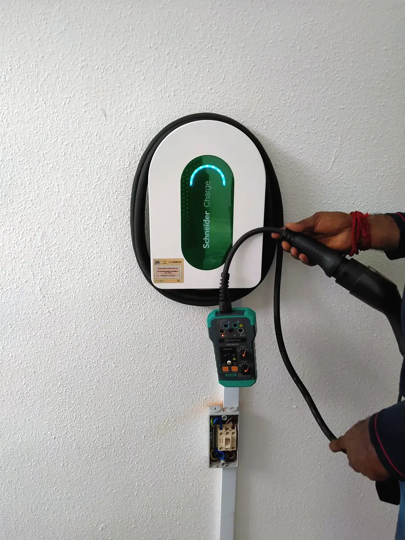 Electrician commissioning a Schneider Charge wallbox with a test instrument connected below it.