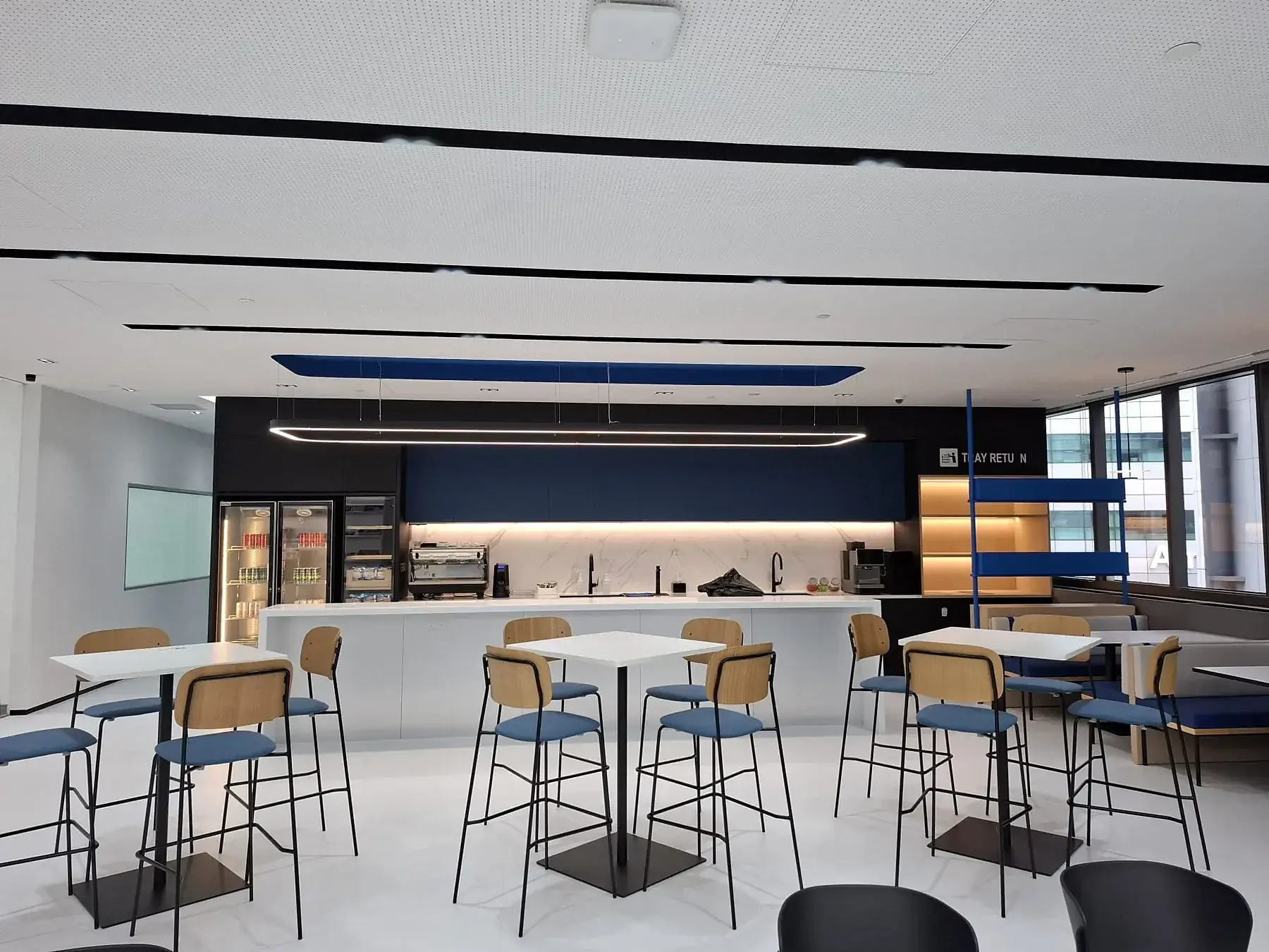 Finished staff cafe with pendant lighting over an island counter and backlit display shelving.