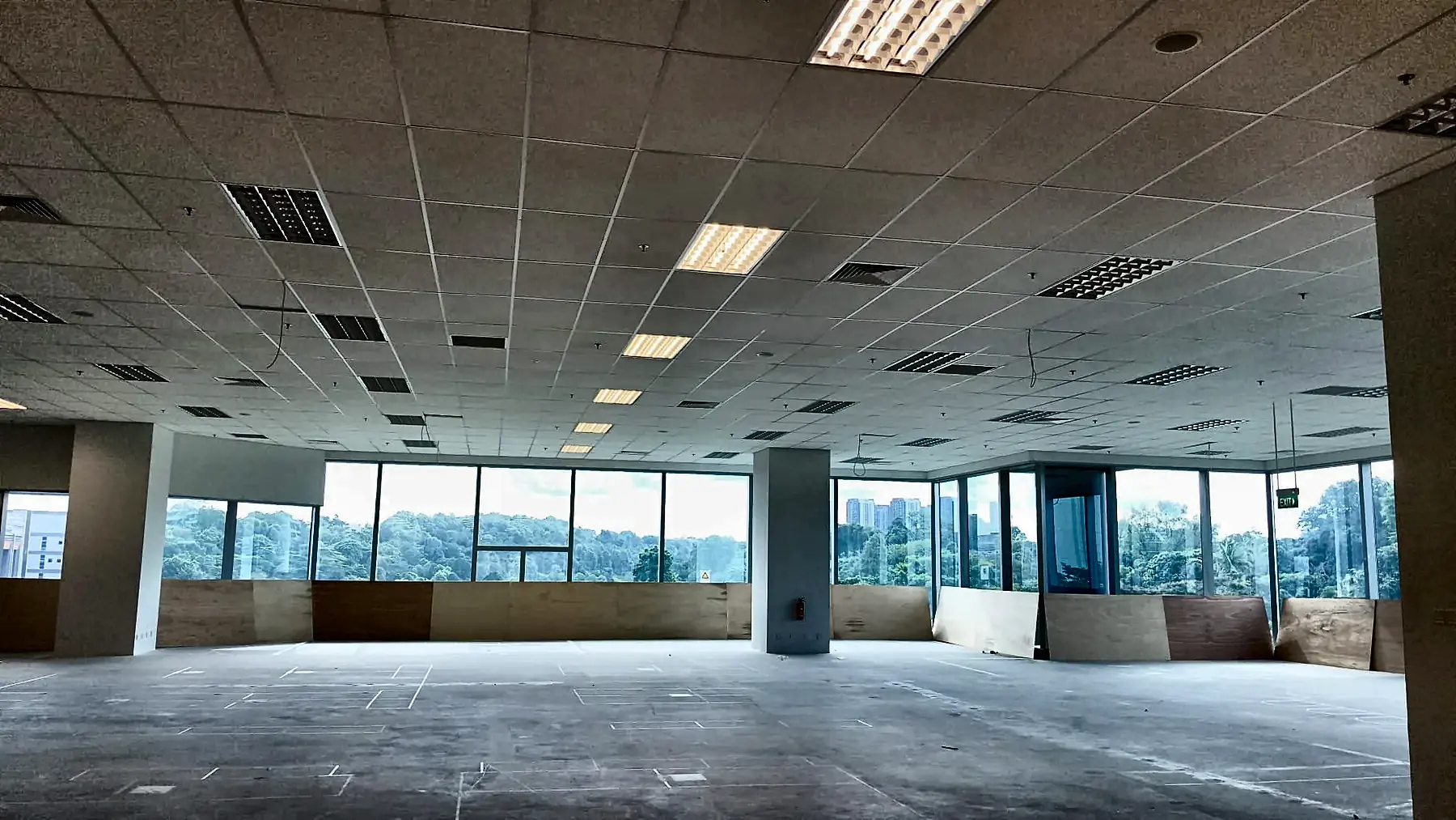 Large open office floorplate with ceiling lighting energised and full-height glazing beyond.