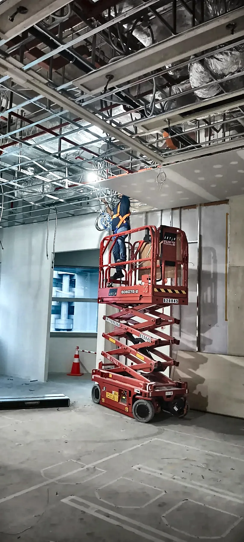 An electrician on a scissor lift installing cabling in an open ceiling above an office fit-out