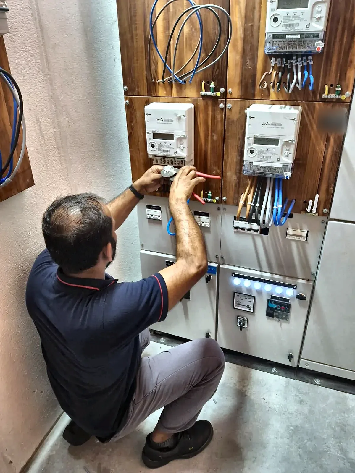 Electrician terminating and testing at a meter board carrying two energy meters.