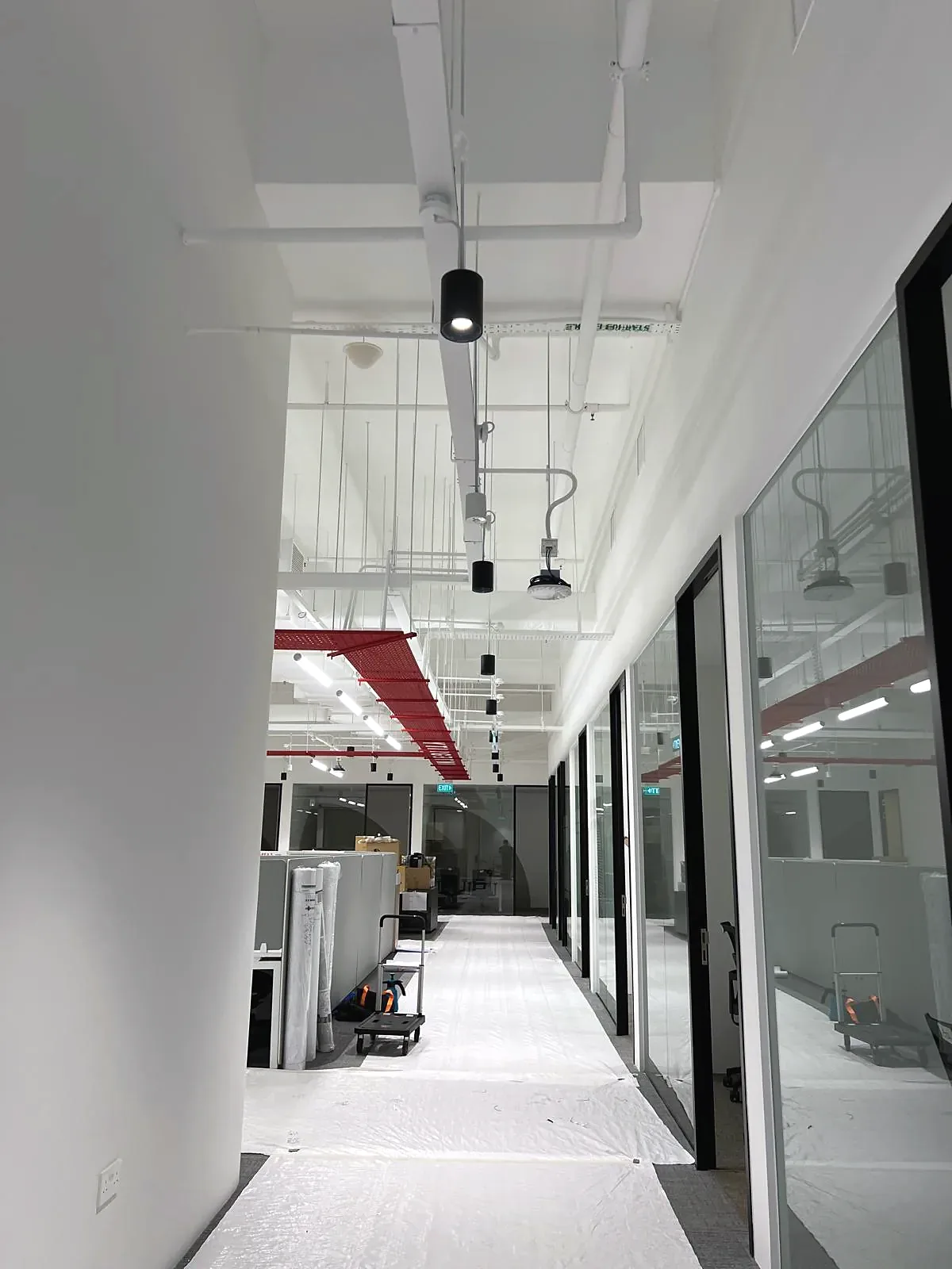 Corridor with painted exposed services overhead and surface-mounted spotlights on track.